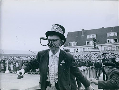Fotografia de epocă a unui bărbat cu ochelari mari, o pălărie și pe costum este urmărită și înconjurată de o mulțime de oameni